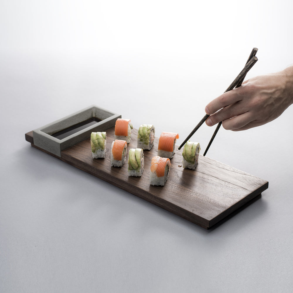Komolab Concrete And Walnut Wood Appetizer Tray With Sushi And A Hand With Chopsticks