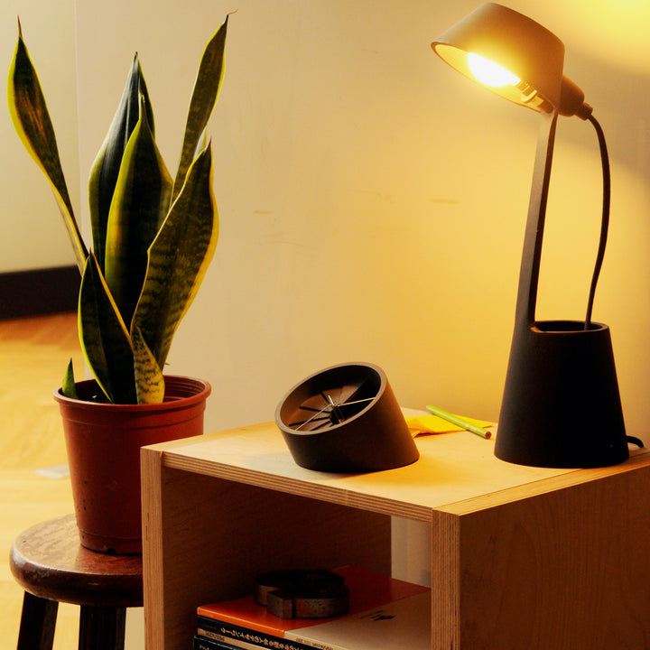 Table clock on a side table with a lamp and plant