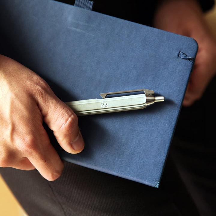 Person Holding a Blue Notebook and Concrete Ballpoint Pen